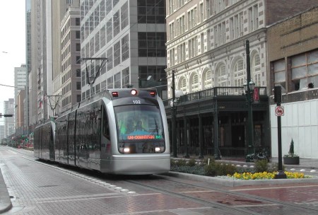 Two-car Houston MetroRail light rail train glides northbound in reservation along Main St. Notice landscaping in median, where station platforms are also placed. Photo: Mike Harrington.