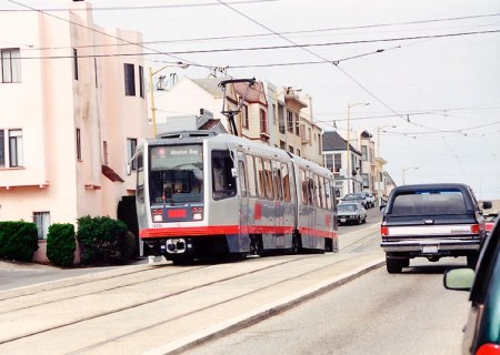 In this view of a train near 15th Avenue, the slightly raised center median reservation can be seen more clearly. Over the train, transverse spanwires holding OCS can be seen; other cross-wires are general utility cables. Photo (copyright) Eric Haas.