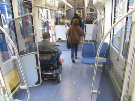 Passenger in wheelchair easily maneuvers chair into accessible space aboard car. In contrast to buses — no tiedowns, no operator assistance needed, no passengers ousted from their seats! Photo: L. Henry.